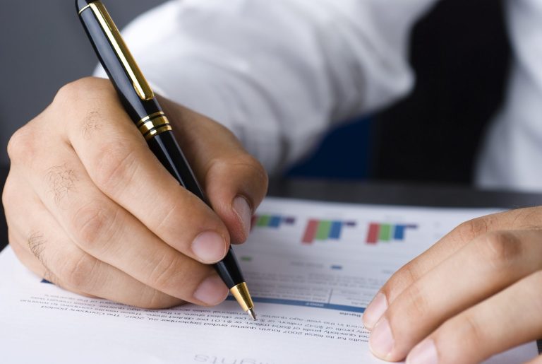 Objektprüfung Eine Hand hält einen Stift über ein Dokument mit Diagrammen und Text.